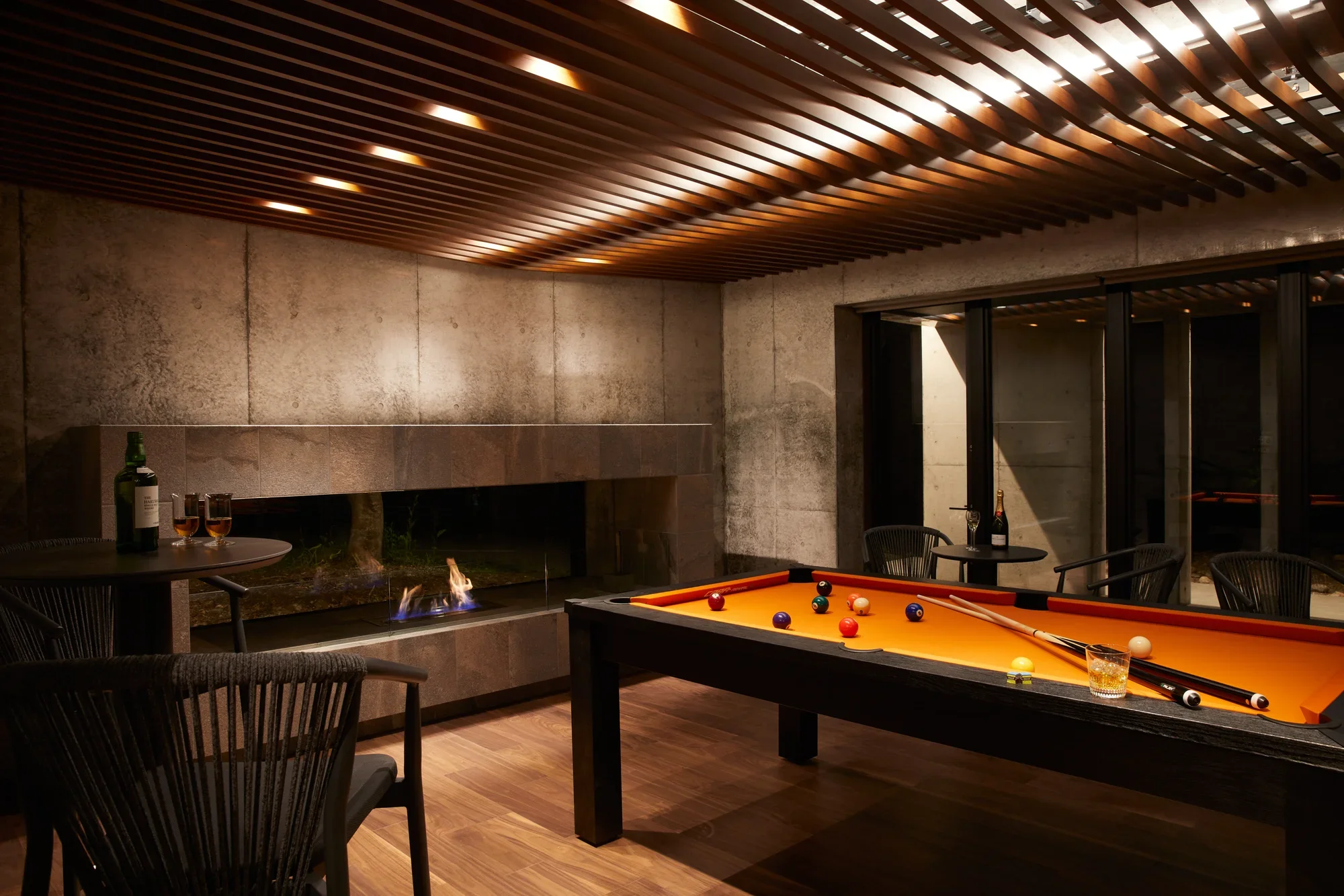 A games room at night with a billiards table, fireplace and glass doors to the garden